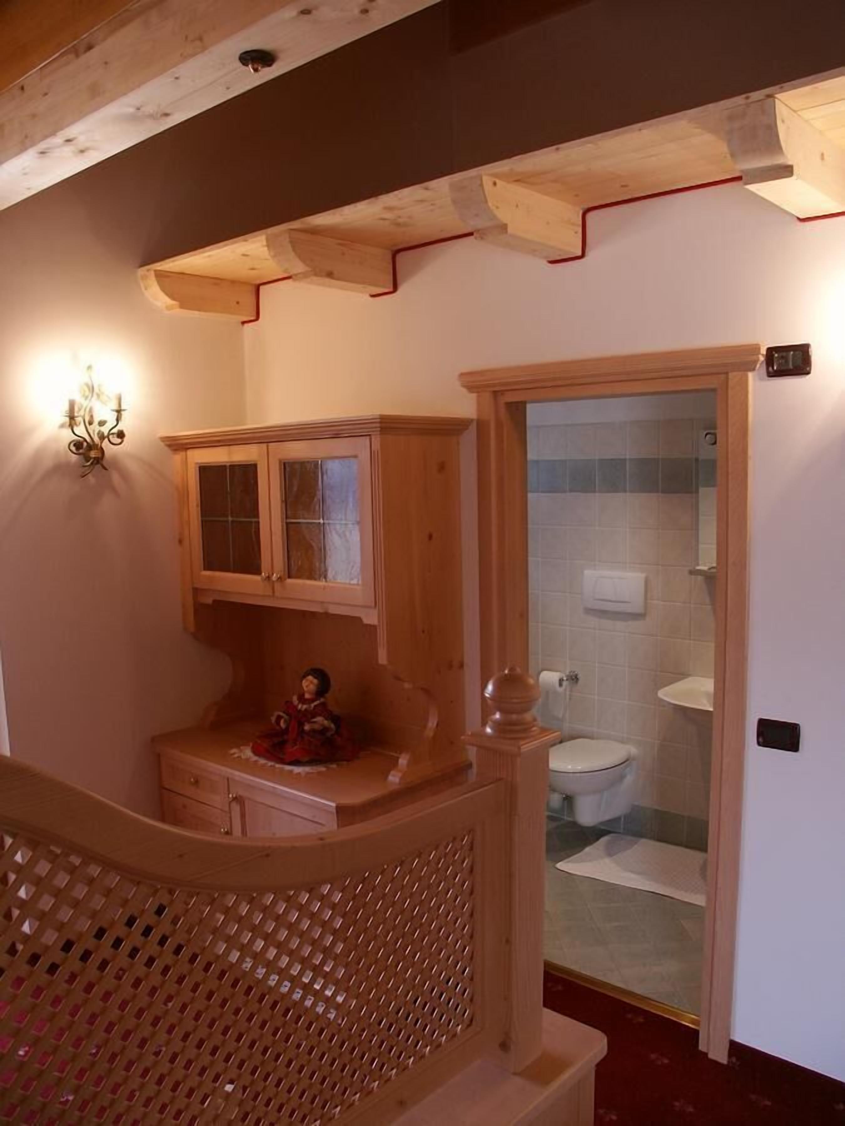 Un bagno in legno con un water, un lavandino e una doccia. Si nota un armadietto in legno sopra il lavandino e un lampadario sulla parete.