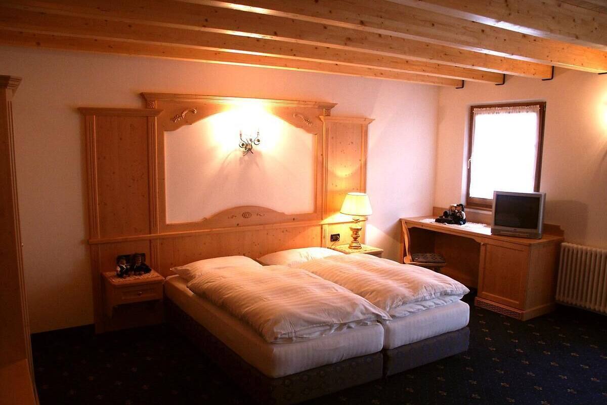 Una habitación con una cama doble, cabecera de madera, mesita de noche con lámpara, televisor sobre un mueble bajo y ventana con vistas.