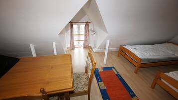 Een kleine, driehoekige slaapkamer op zolder, met een houten bed, een houten tafel en een stoel.