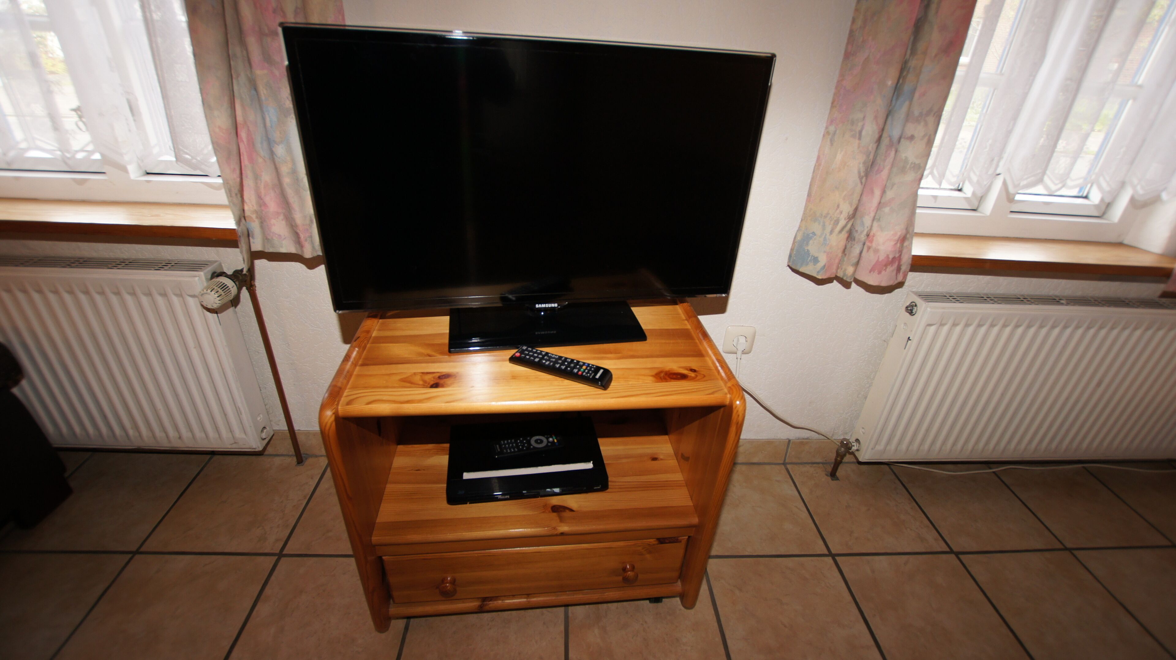 Un mueble bajo de madera con un televisor de pantalla plana, controles remotos y un reproductor de DVD Samsung.