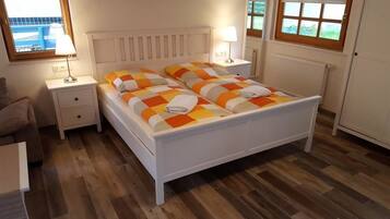 A bedroom with a white bed, two nightstands, a lamp, and a view of the outside.