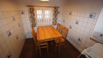 Zona pranzo con tavolo e sedie in legno, una finestra con tende e pareti in piastrelle decorate.