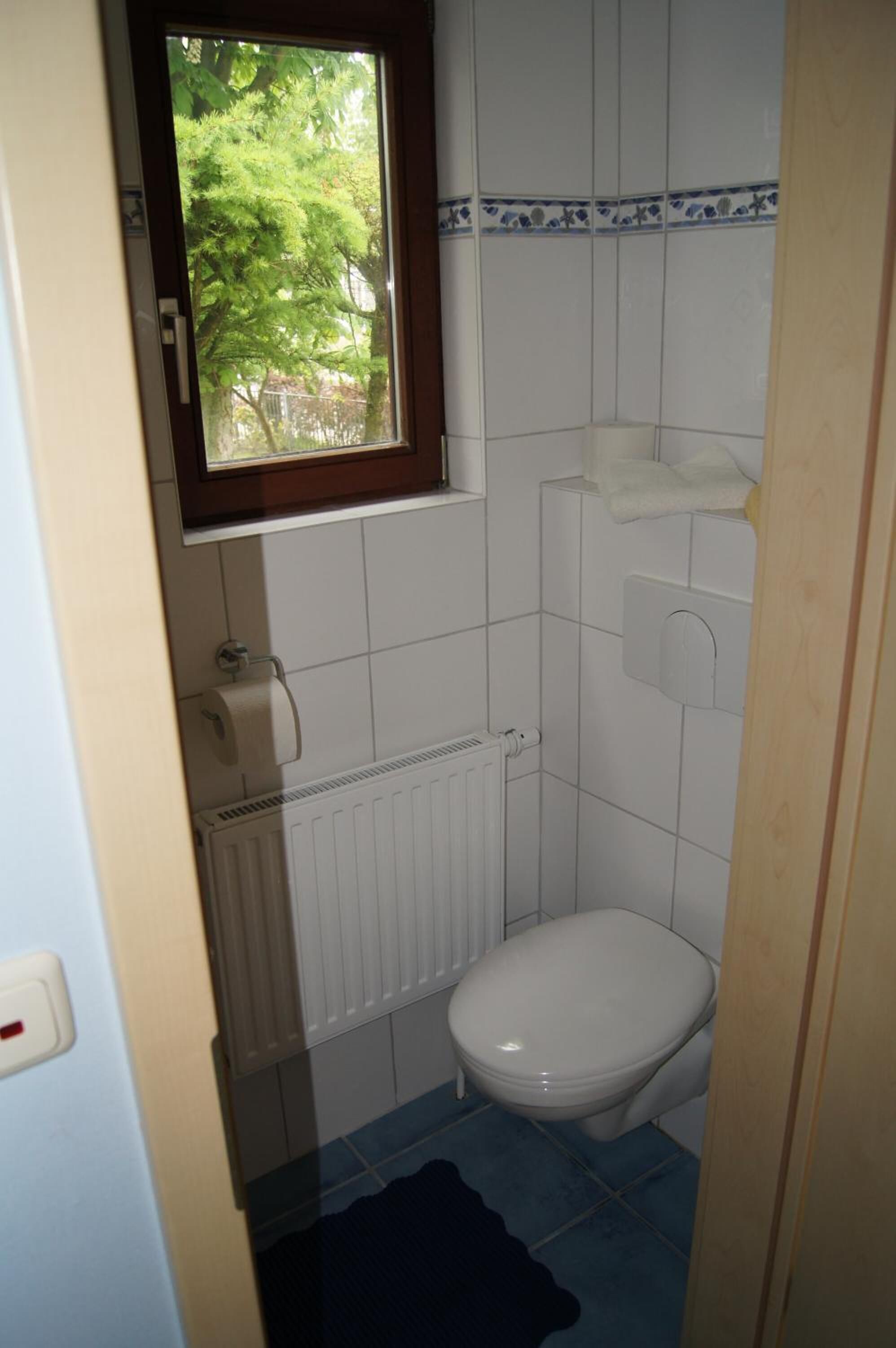 A small, compact bathroom with a toilet, a towel rack, and a window.