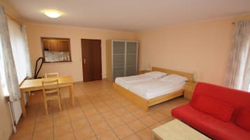 Een slaapkamer met een bed, een rode bank, een houten bureau met stoel, een kledingkast en een zichtbare badkamer door een deur.
