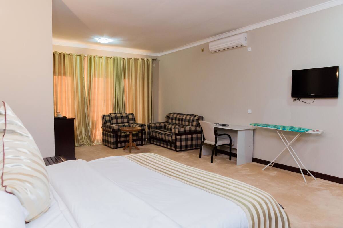 Een hotelkamer met een bed, twee geruite fauteuils, een bureau met stoel, een televisie en een strijkplank.