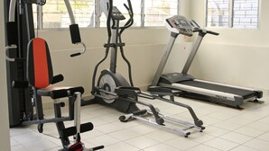 Een sportschool met trainingsapparatuur, waaronder een bank, een elliptische trainer en een loopband.