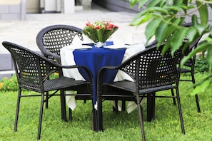 A table set with a blue tablecloth, surrounded by black wicker chairs, and a vase with flowers.