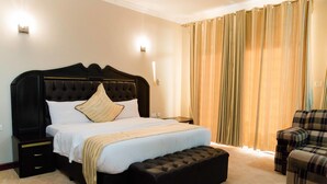 Een verzorgd ingerichte slaapkamer met een groot bed, een nachtkastje, een bankje en een geruite fauteuil.