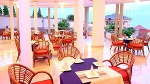 Een restaurant met rieten stoelen en tafels, grote pilaren en uitzicht op zee.