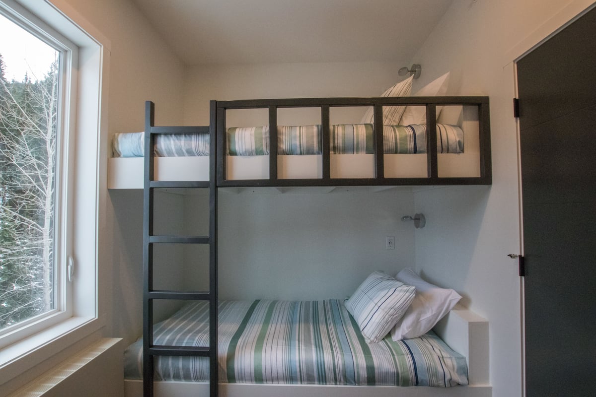 A bunk bed room with a window, a ladder, and a door.