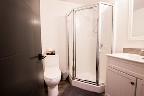 A bathroom with a toilet, a glass-enclosed shower, and a sink with a mirror above it. - The Burfield (Sun Peaks)