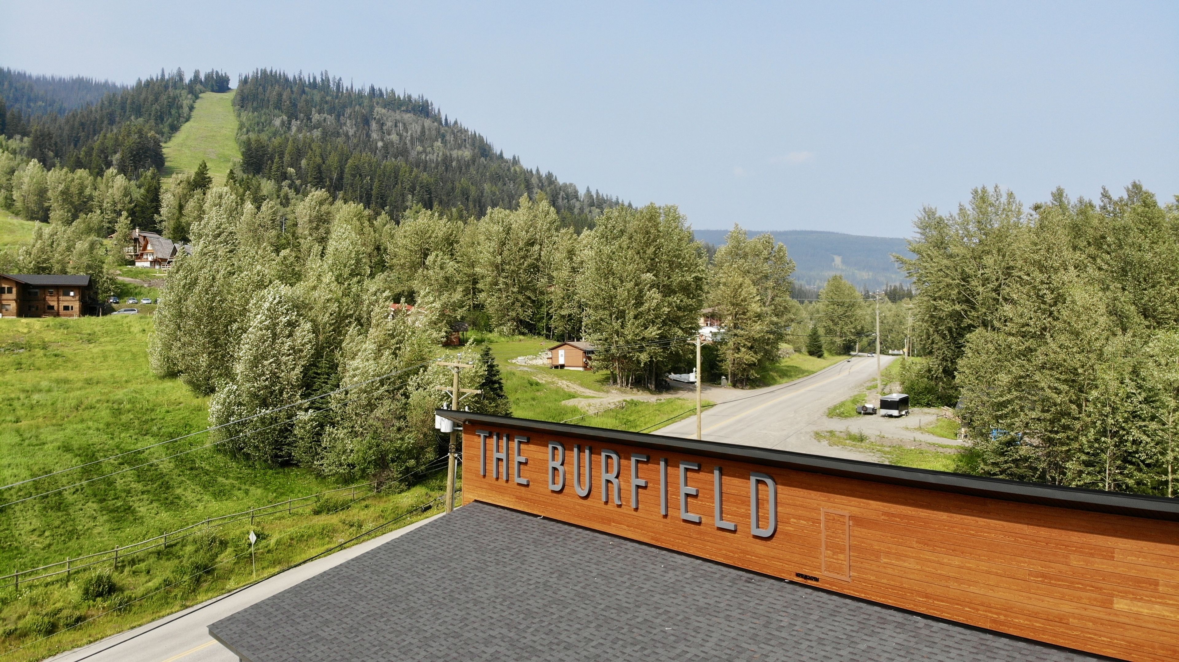 A view of The Burfield, featuring a wooden facade, a paved road, and surrounding greenery.