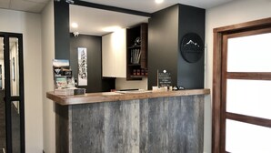 A reception desk with a wooden counter, a mounted sign with a mountain logo, and a framed picture of a snowy mountain. - The Burfield (Sun Peaks)