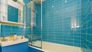 A bathroom with blue tiles, a white sink, and a glass-enclosed shower. - TDM Bachelot Lettings (London)