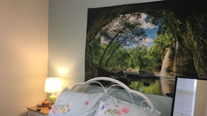 A bedroom with a bed, a nightstand, a lamp, and a large nature-themed painting on the wall. - TDM Bachelot Lettings (London)