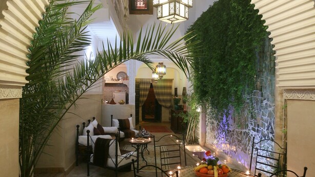 An indoor dining area with a round table surrounded by chairs, a decorative centerpiece, and a wall with a climbing plant. - Riad El Bellar (Marrakech)