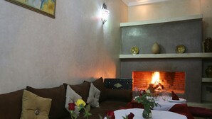 A cozy living room with a fireplace, a sofa with cushions, and a dining table set for two. - Riad El Bellar (Marrakech)