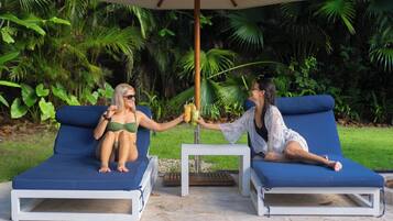 Two lounge chairs under a canopy, surrounded by lush greenery.