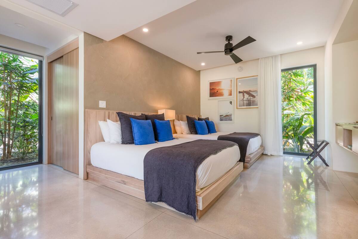 Een moderne slaapkamer met een groot bed, een kleiner bed en een plafondventilator.