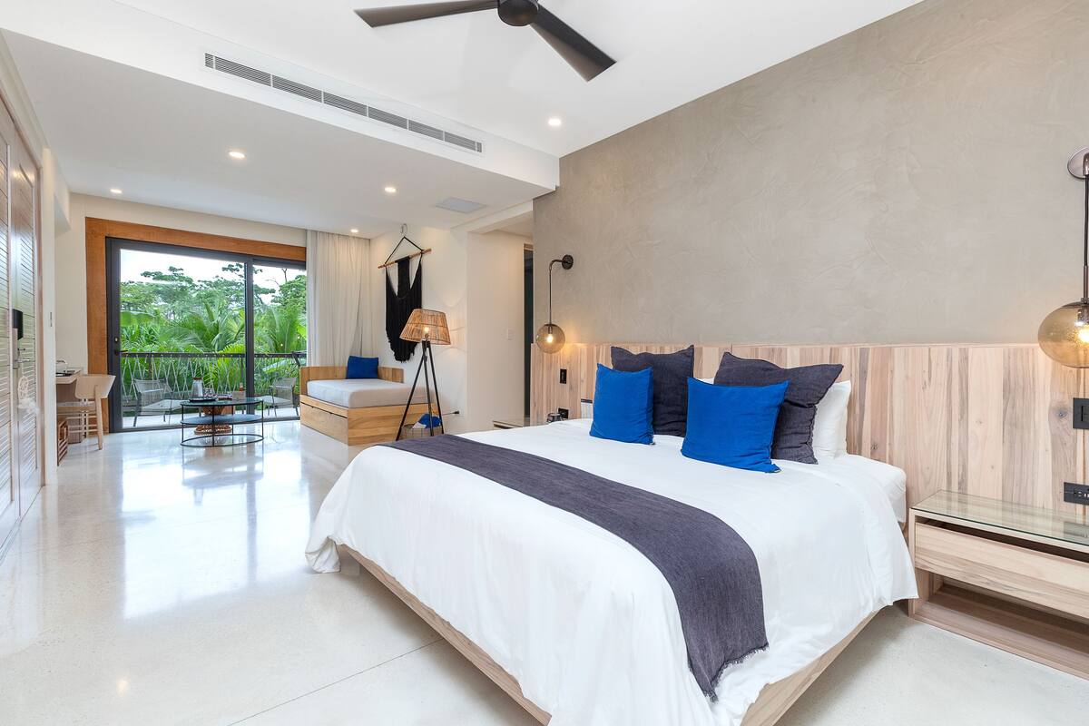 Een moderne slaapkamer met een groot bed, een plafondventilator en uitzicht op groen door het raam.
