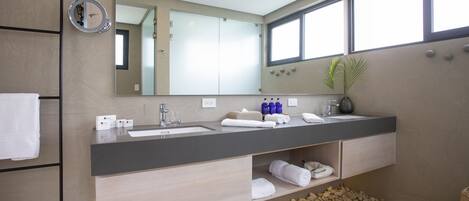 A modern bathroom with a large mirror, two sinks, a towel rack, and a plant.