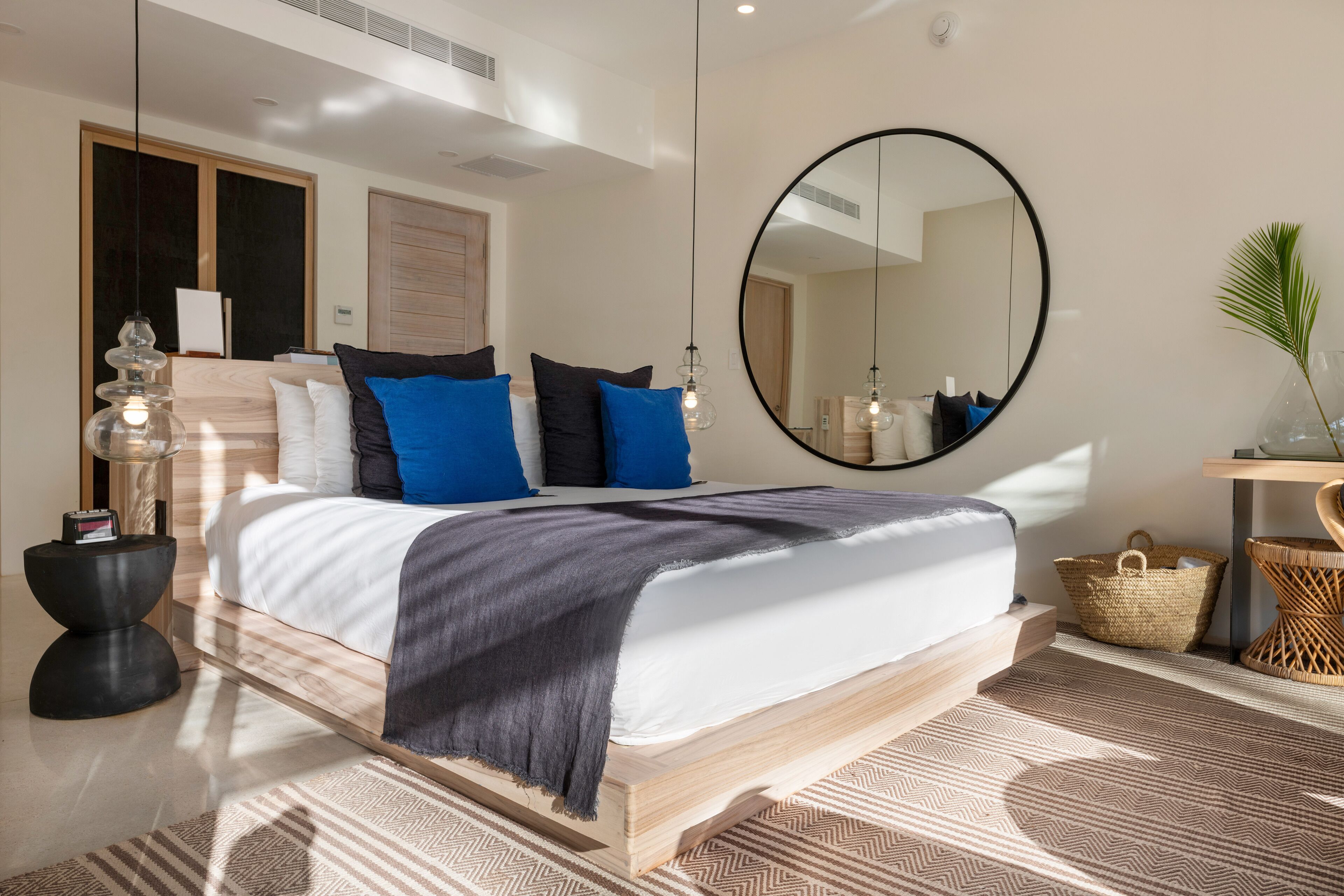 A modern bedroom with a wooden bed, a large round mirror, and a bedside table with a lamp.