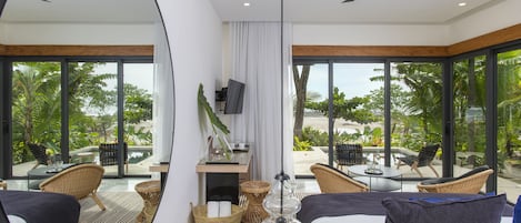 Une chambre d’hôtel moderne dotée d’un grand lit, d’un ventilateur de plafond, d’une télévision et offrant une vue sur la plage et les palmiers.