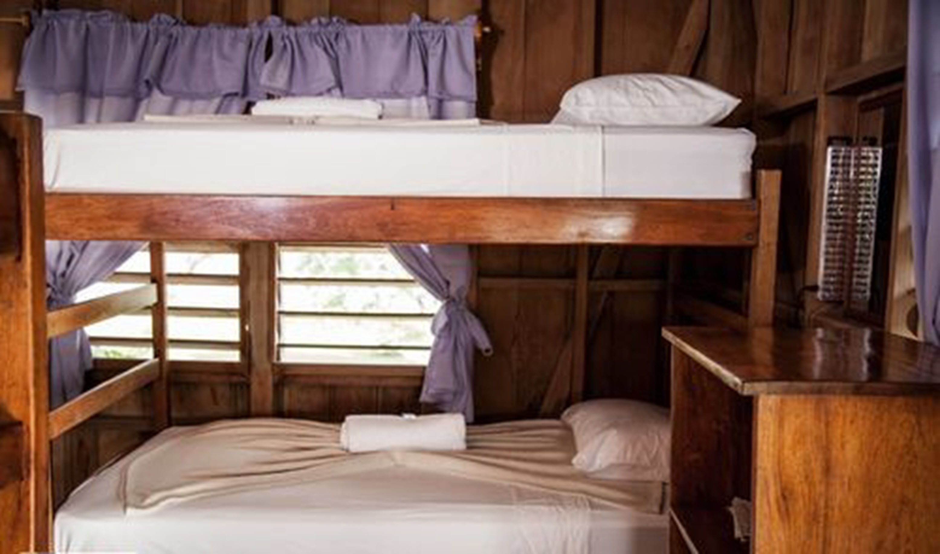 A bunk bed room with a wooden structure, a small table, and a window with curtains.