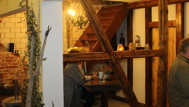 A rustic interior with exposed wooden beams, a brick wall, and a staircase leading to an upper level. - Landhaus Tewel (Neuenkirchen)