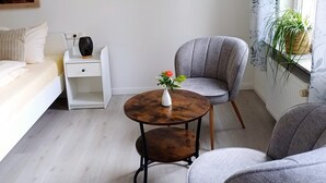 A modern living room with a sofa, two grey armchairs, a small round table with a vase, and two wooden shelves with decorative items. - Landhaus Tewel (Neuenkirchen)