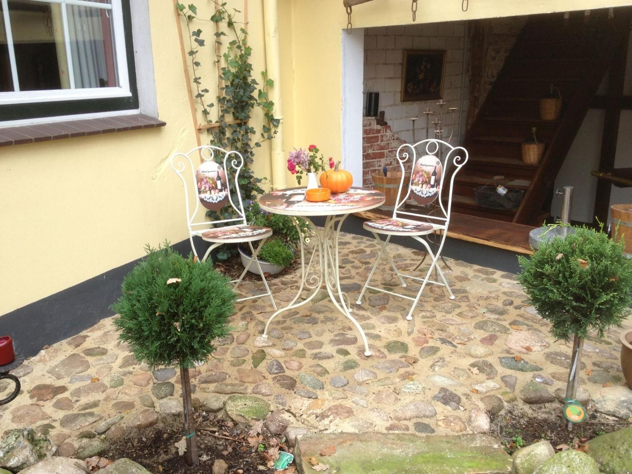 Eine Terrasse mit einem runden Tisch und zwei Stühlen, umgeben von kleinen Topfpflanzen.