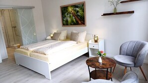 A modern bedroom with a bed, bedside tables, a chair, a small table with a vase, and a painting on the wall. - Landhaus Tewel (Neuenkirchen)