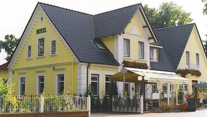 A yellow building with a sign reading "HOTEL" and a covered outdoor seating area. - Landhaus Tewel (Neuenkirchen)