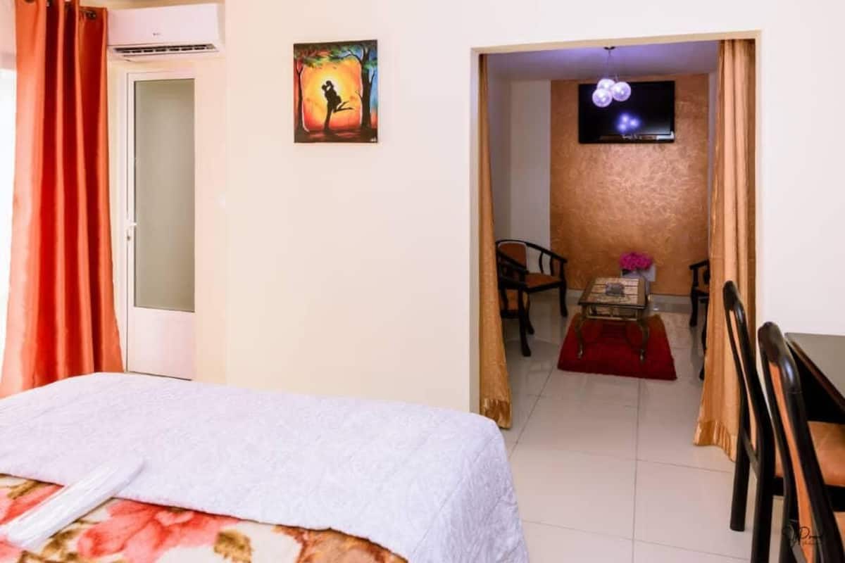 Quarto de hotel com cama, televisão, pintura e área de refeições com cadeiras e mesa.