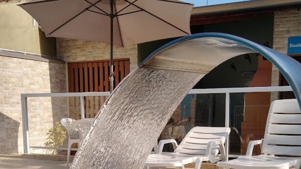 An outdoor seating area with white plastic chairs and a large umbrella. - Canto Verde Aptos III (Caraguatatuba)
