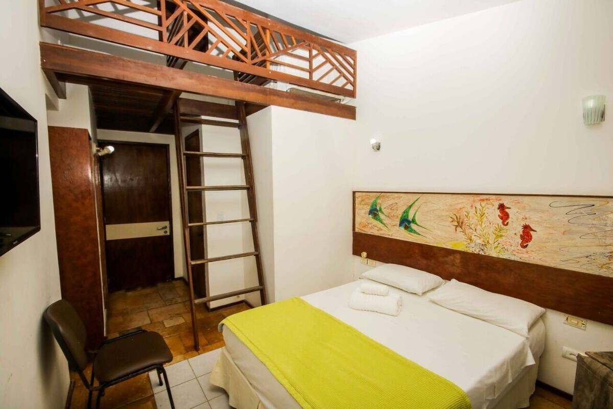 A bedroom with a bunk bed, a ladder, a desk, and a bed with a green blanket.