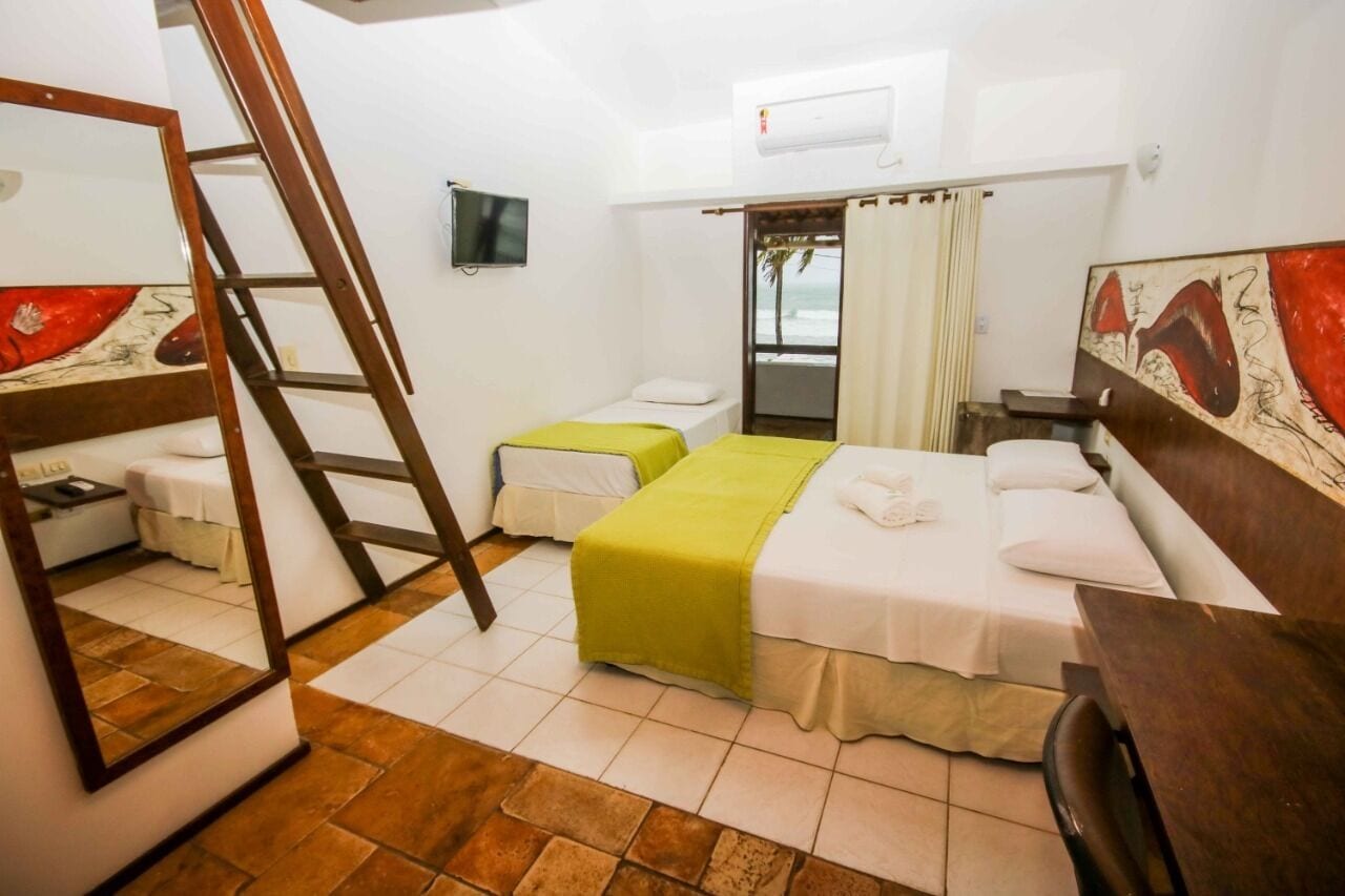 A hotel room with two beds, a TV, a window with curtains, and a wooden ladder.