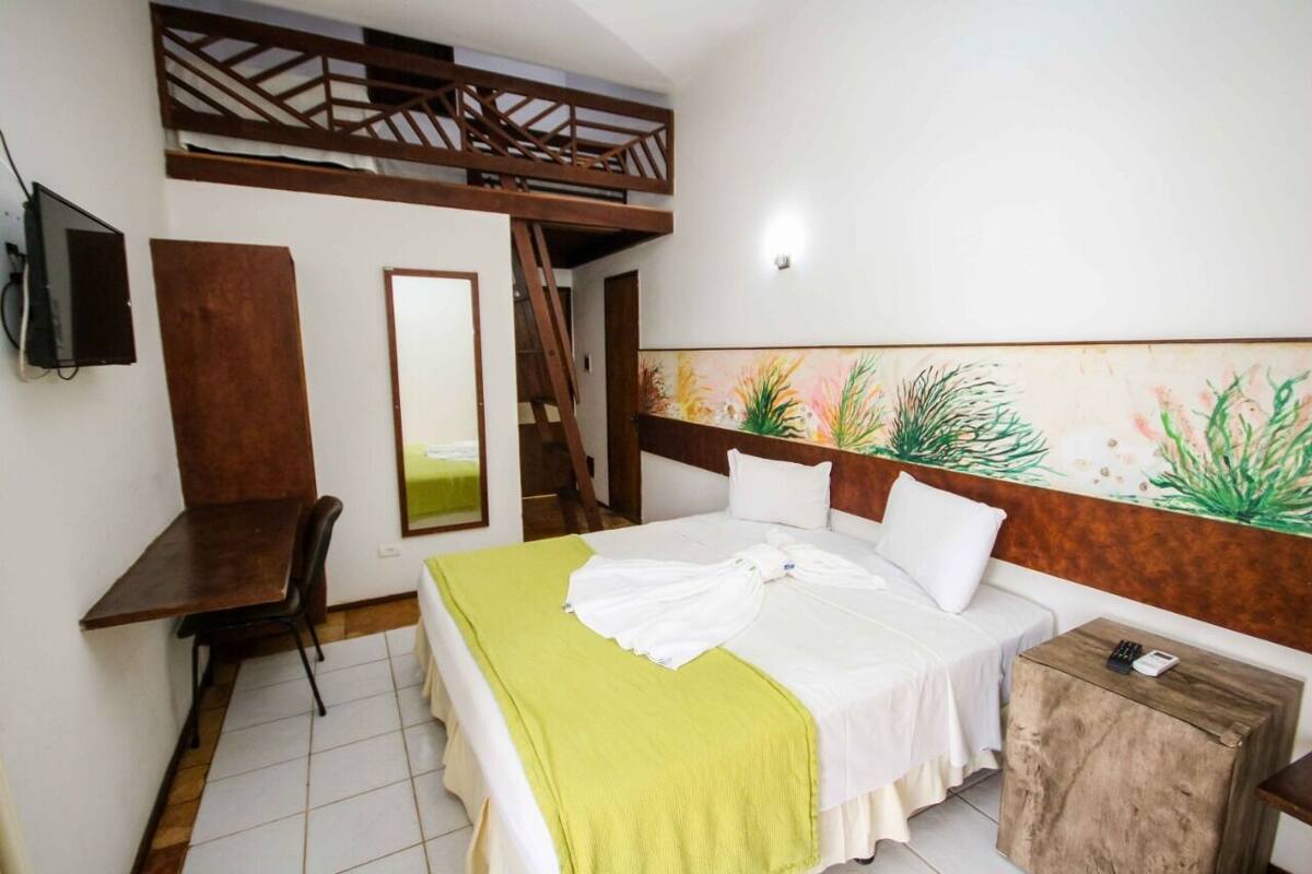 A bedroom with a bunk bed, a desk, a chair, a bed with a green blanket, and a wall with a plant mural.