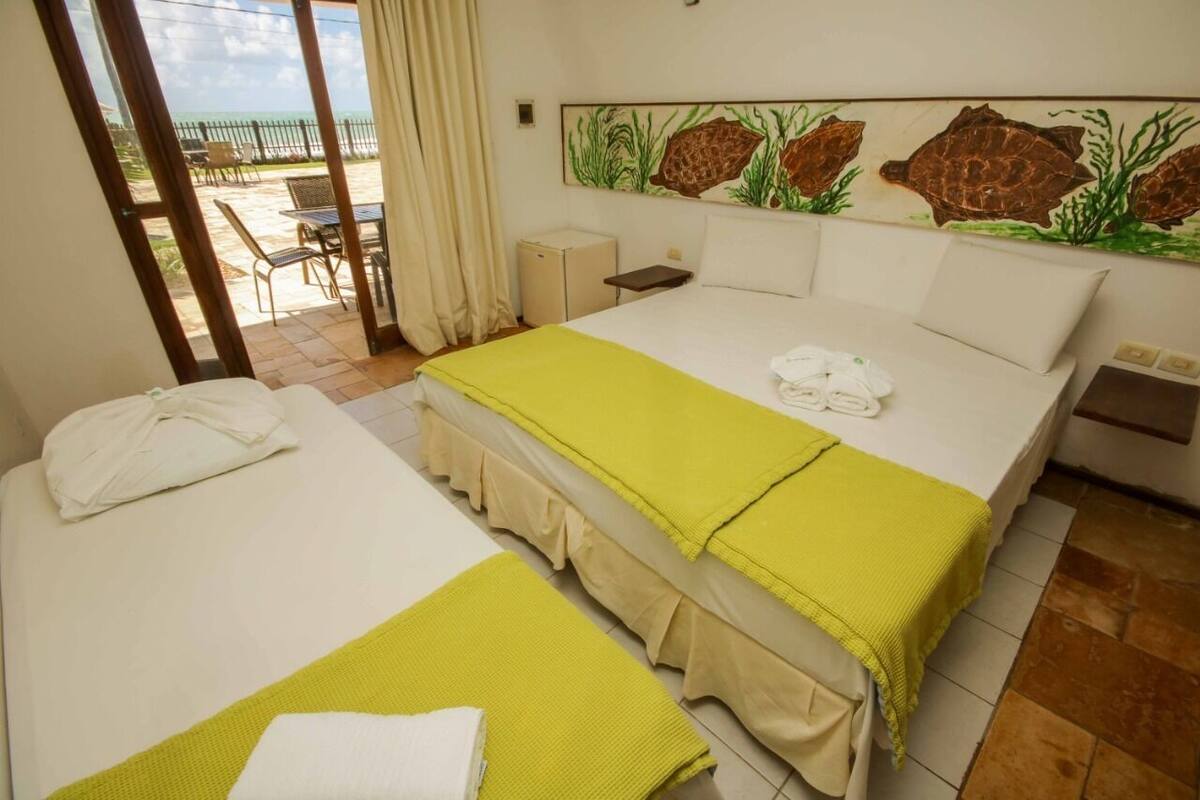 A hotel room with two beds, a view of the beach, and a painting of sea turtles on the wall.