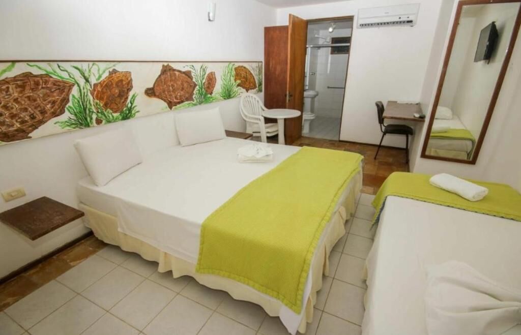 Une chambre d’hôtel avec un grand lit, un plus petit lit, un bureau, une chaise et une salle de bain visible à travers une porte ouverte.