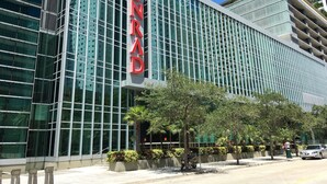 A modern hotel with a prominent 'CONRAD' sign, large glass windows, and a well-maintained outdoor area with trees and a parked car. - 1 Bedroom Brickell Condo (Miami)