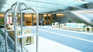 A spacious lobby with a modern design, featuring a central seating area with sofas and a coffee table, a reception desk, and a glass elevator. - 1 Bedroom Brickell Condo (Miami)