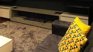 A modern living room with a flat-screen TV mounted on a dark wall, a fireplace below, and a sofa with a patterned cushion.
