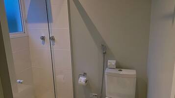 A small, modern bathroom with a glass shower enclosure, a toilet, and a trash bin.