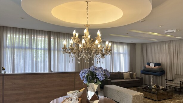 A modern living room with a chandelier, a round table with a vase of flowers, a sofa, and a coffee table.