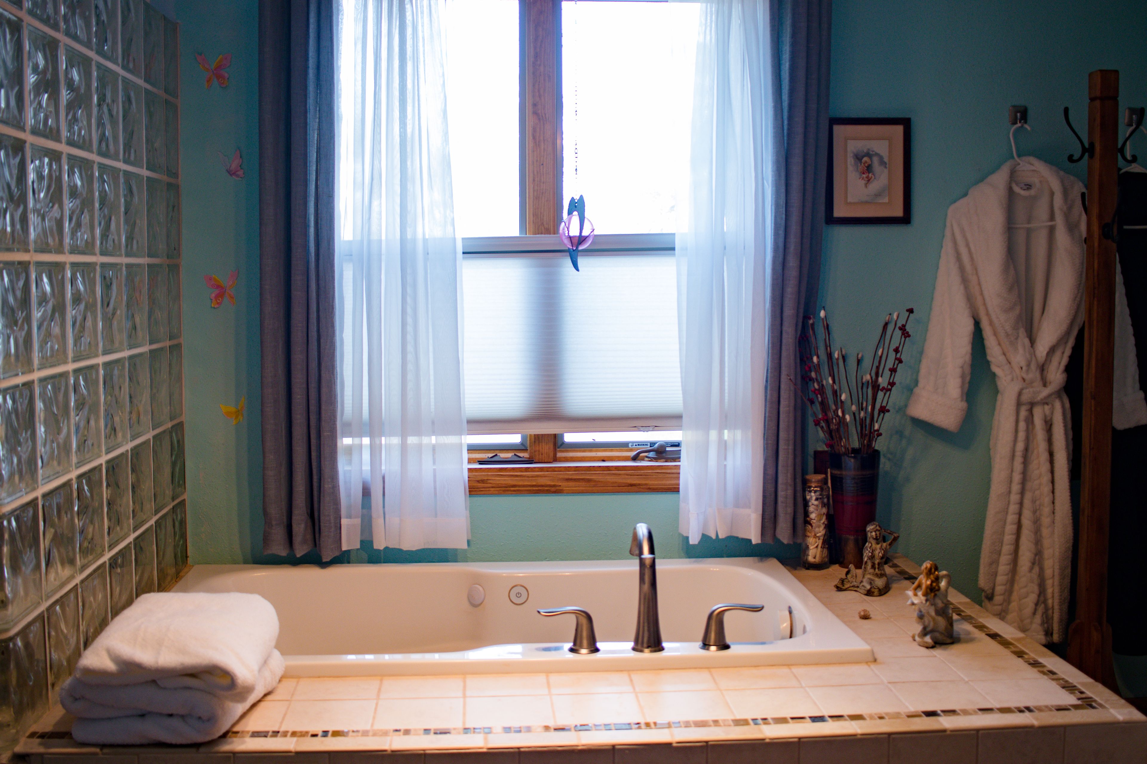 Un baño con bañera, una ventana con cortinas, un montón de toallas y un tapete de baño de madera.