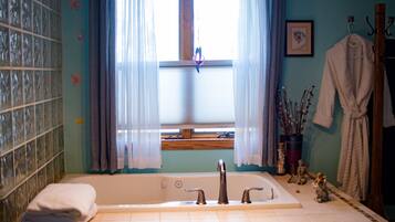Un baño con bañera, una ventana con cortinas, un montón de toallas y un tapete de baño de madera.