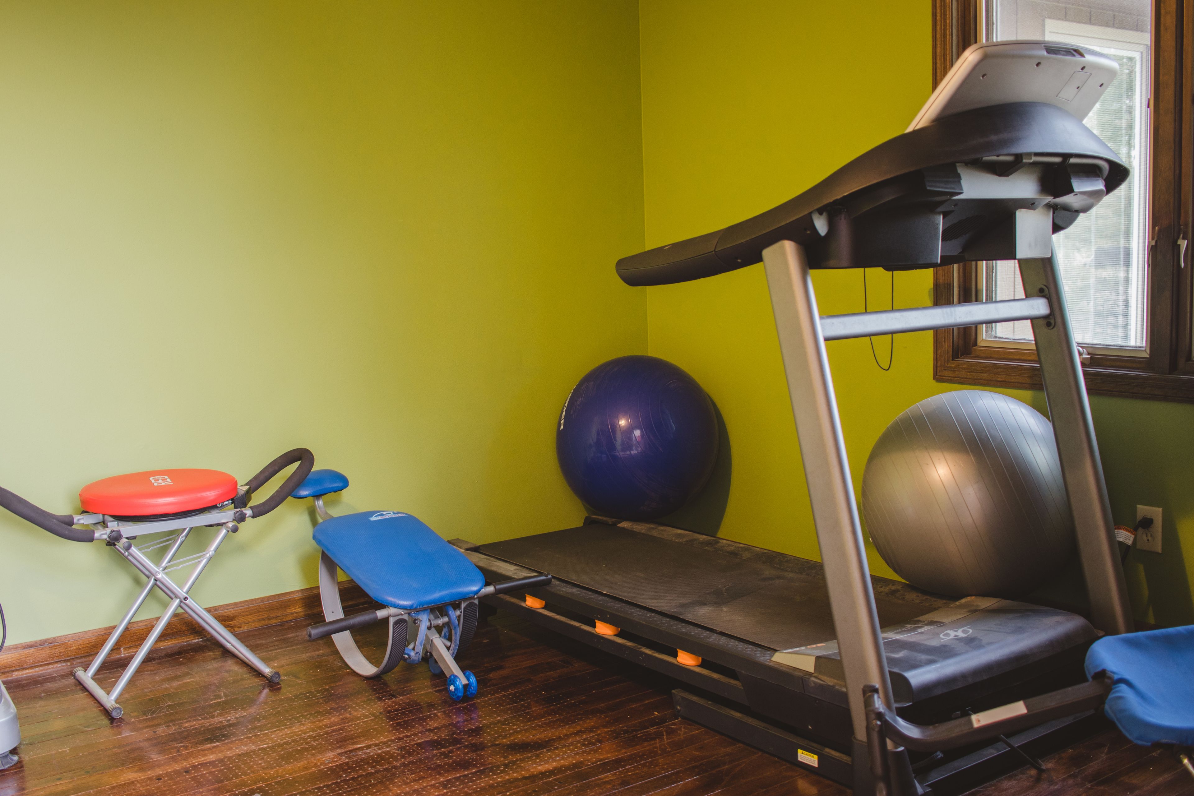 Una habitación con una cinta de correr, una pelota de ejercicios y una silla azul.