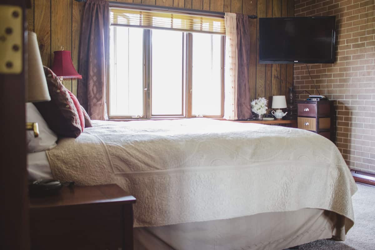Un dormitorio con una cama grande, un televisor montado en la pared y una ventana con cortinas.