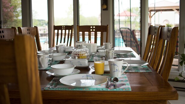 A dining table set for breakfast with chairs, plates, cups, and a glass of orange juice. - Shane Acres Country Inn (Juneau)